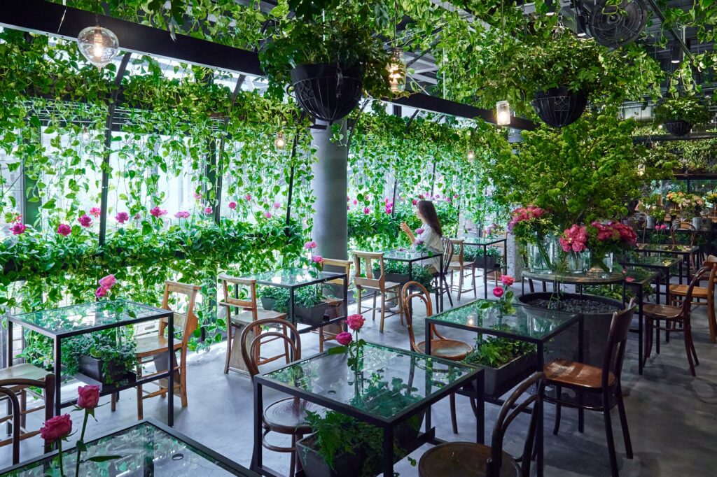 天井から吊られた緑とつる性植物が店内を覆い、テーブル席が並ぶ空間(グリーンハウス)
